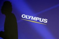 A staff member is silhouetted on a projector screen displaying a logo of Olympus Corp before a news conference in Tokyo February 13, 2012. REUTERS/Yuriko Nakao