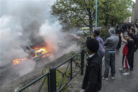 Bystanders take photos of a row of burning cars in the suburb of Rinkeby after youths rioted in several different suburbs around Stockholm, late May 23, 2013 in this picture provided by Scanpix. REUTERS/Fredrik Sandberg/Scanpix