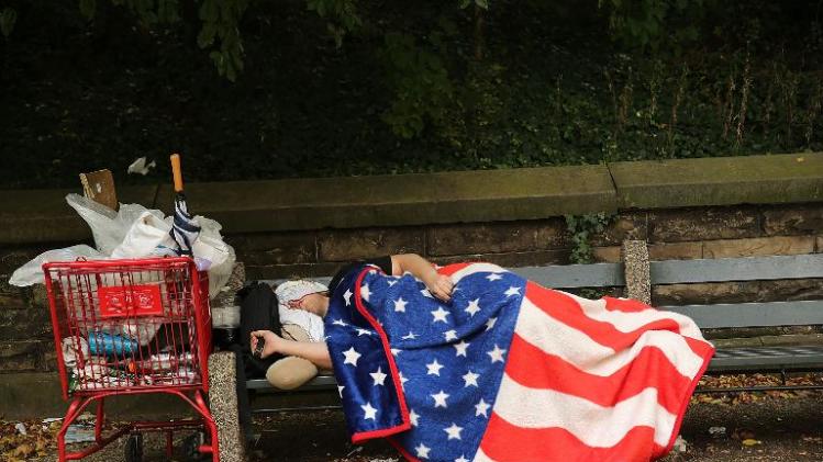 A homeless man sleeps under an American Flag blanket on a park bench on September 10, 2013 in the Brooklyn borough of New York City