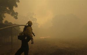 A fire fighter carries a hose as he watches a fire &hellip;