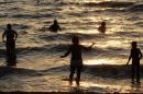 Tourists enjoy a day at the beach as the sun sets over the Dead Sea
