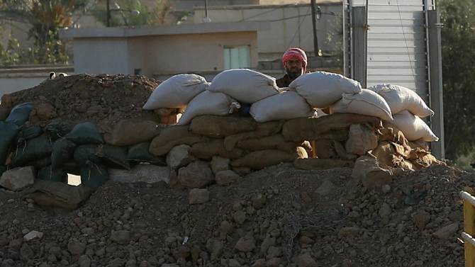 Militant with the Islamic State group peers from behind a barricade at a Kurdish peshmerga position near the Mullah Abdullah Bridge, located on the road between Irbil and Kirkuk, 290 kilometers (180 miles) north of Baghdad, Iraq, Saturday, Sept. 27, 2014. Over a wall of dirt bags across the Mullah Abdullah Bridge in northern Iraq, a militant with the Islamic State group looks at Kurdish fighters stationed on the other side of the bridge. (AP Photo/Hadi Mizban)