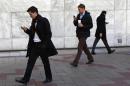 Workers look at their phones while walking at the Canary Wharf business district in London