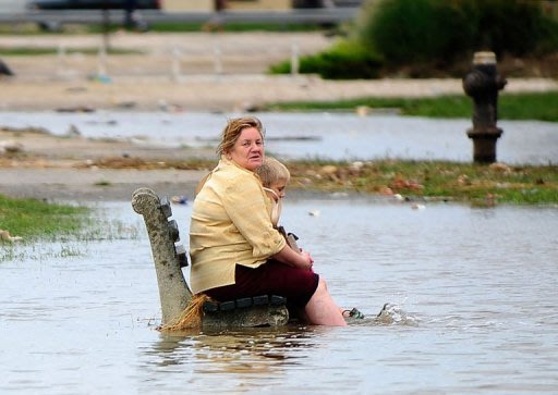 A woman and a child sit on a public bench amid floodwater