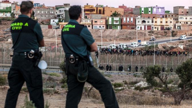 Spanish Guardia Civil watch as would-be immigrants from Africa sit atop a fence on Spain&#39;s tiny north African territory of Melilla on August 13, 2014