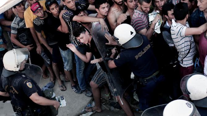 A policeman pushes a migrant as hundreds wait to complete a registration procedure at a stadium on the Greek island of Kos on August 12, 2015