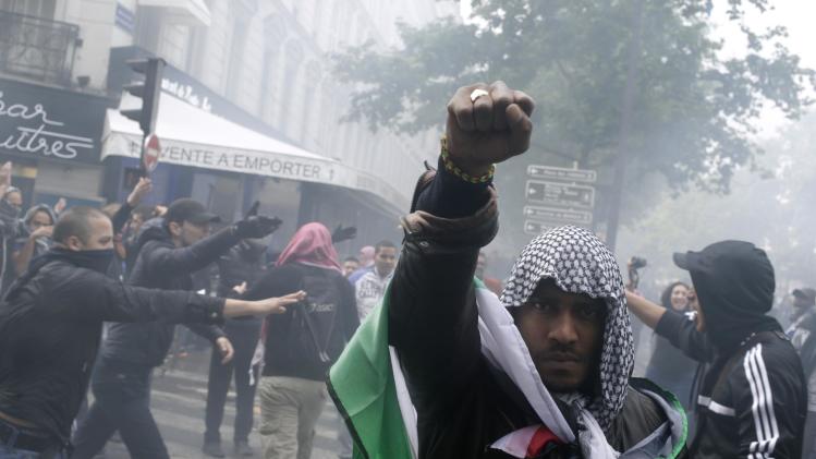 A protester wearing a kaffiyeh and wrapped in a Palestinian flag raises his fist on July 13, 2014 in Paris