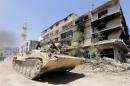 Syrian government troops sit atop a tank as they drive past a damaged building in Mleiha on the outskirts of the capital Damascus on August 15, 2014