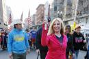 Boston Marathon bombing survivor Heather Abbott carries a symbolic torch as she crosses the marathon finish line in Boston, Sunday, April 13, 2014, for the last leg of a cross country charity run that began in March in California. Abbott, along with other survivors and family members joined the relay runners for the final half-block to the finish. (AP Photo/Michael Dwyer)