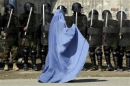 File photo of woman walking past riot police outside a gathering in Kabul's stadium