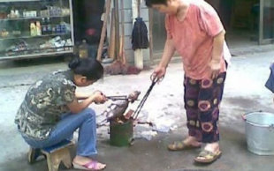 Two women seen roasting the puppy using what looks like a portable stove. (Screengrab from ww.chinasmack.com)