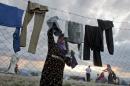 A woman hangs her clothes to dry on a barbed wire fence at the migrants camp in Idomeni, Greece, Thursday, May 19, 2016. Thousands of stranded refugees and migrants have camped in Idomeni for months after the border was closed. (AP Photo/Darko Bandic)
