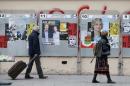 People walk past campaign posters of candidates from the Ile de France region which are glued on metallic electoral panels near a voting station ahead of the upcoming French regional elections in Paris