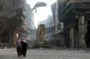 Syrians walk past anti-sniper curtains on May 12, 2014 in a destroyed neighbourhood of the Old City of Homs