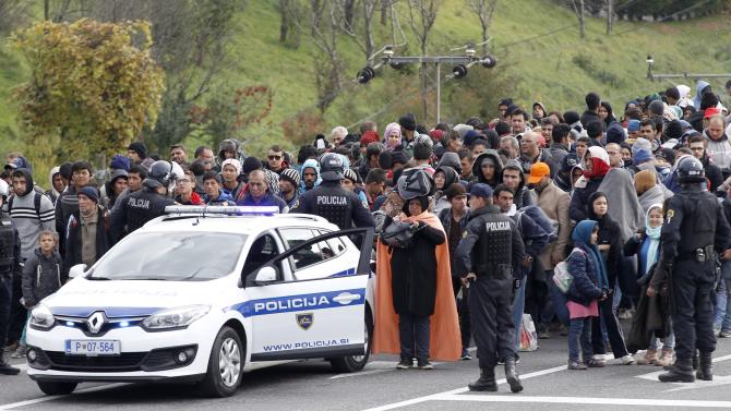 Slovenian policemen escort a group of migrants from a train towards a camp in Sentilj, Slovenia, Friday, Oct. 23, 2015. Thousands of people are trying to reach central and northern Europe via the Balkans but often have to wait for days in mud and rain at the Serbian, Croatian and Slovenian borders.  (AP Photo/Petr David Josek)