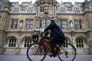 A woman rides a bike next to the Oriel College building with the statue of Cecil Rhodes on its facade in Oxford
