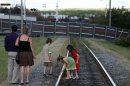 Children touch the lines of a railway track as it leads to a fence erected to block the view of the wreckage from a train derailment in the town of Lac Megantic