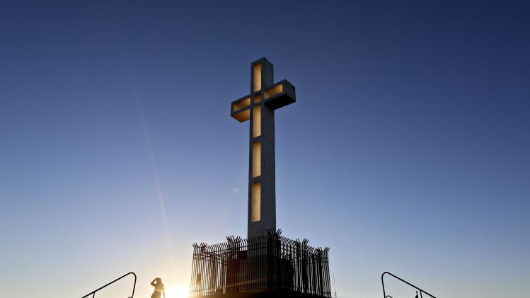People gather in the late evening sun around the massive cross sitting atop the Mt. Soledad War Memorial in La Jolla