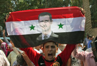 In this photo taken on a government-organized tour, a Syrian man shouts in support of President Bashar Assad, seen on the flag, as residents cheer for Syrian soldiers leaving the eastern city of Deir el-Zour, Syria, Tuesday, Aug. 16, 2011. State-run news agency SANA said army units began withdrawing from Deir el-Zour Tuesday after ridding the city of "armed terrorist gangs" in an operation that lasted several days. (AP Photo / Bassem Tellawi)