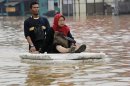 A woman sits on a makeshift raft as she crosses a flooded road in Jakarta