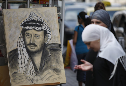 A Palestinian woman stands by a drawing of late Palestinian leader Yasser Arafat, displayed on a street corner in the West Bank city of Ramallah, Thursday, July 5, 2012. Palestinian President Mahmoud Abbas has said he's willing to exhume the body after doctors said they found elevated levels of the radioactive agent polonium-210 on clothing reportedly worn by Arafat before his death in November 2004. However, Abbas aide Nimr Hamad said Thursday the Palestinian leader first wants to send experts to Europe to learn more from the Swiss lab and to the French military hospital where Arafat died. (AP Photo/Majdi Mohammed)