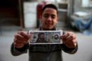 A boy poses while showing one of the fake U.S. 100 dollar banknotes depicting Islamic State's leader Abu Bakr al-Baghdadi and al-Nusra Front's leader Abu Mohammed al-Joulani, that were dropped by Syrian army jets in the Douma neighborhood of Damascus