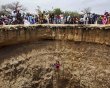 People watch a man descend into a large former well during a traditional ceremony in the village of Ndande