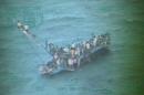 This image taken from video made available by the U.S. Coast Guard shows a group of Haitian migrants sitting on the hull of a capsized sailboat near Staniel Cay, Bahamas, Tuesday, Nov. 26, 2013. Bahamian authorities have confirmed that at least 20 people died when the boat flipped over near Staniel Cay. Interviews with migrants suggest the toll could reach about 30 people. The overloaded sailboat apparently struck a reef and capsized near tiny Harvey Cay, west of Staniel Cay in the Exumas. (AP Photo/U.S. Coast Guard)