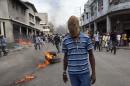A masked protester walks in the street where burning tires were set up by protesters demanding the resignation of President Michel Martelly in Port-au-Prince, Haiti, Sunday, Jan. 11, 2015. At the same time, Martelly and opposition officials were locked again in negotiations at a hotel, trying to forge a last-minute deal to resolve a standoff stalling elections. Martelly will rule by decree if they don't resolve the political crisis by the end of Monday. (AP Photo/Dieu Nalio Chery)