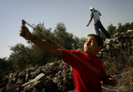 FILE - A palesztin fiú használ csúzli, hogy átkot köveket izraeli csapatok nem látott, közben tiltakozást építése ellen Izrael kerítés a ciszjordániai faluban Bil'in péntek 20 május 2005.  Az elmúlt öt éves az izraeli hadsereg őrizetbe vett több száz palesztin gyermekek dobott sziklák izraeli katonák, kihallgatták őket, és börtönbe számos, a jogi csoport szerint a kiadott jelentés hétfő július 18, 2011.  B'Tselem, egy izraeli csoport, amely figyeli az emberi jogok megsértése a palesztin területeken, felszólította a katonai módot végrehajtás megfelel a kor a gyanúsítottak.  (AP Photo / Emilio Morenatti, File)
