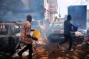 Two men walk next to burned cars in Conakry on May 7, 2015 during clashes between anti-government demonstrators and police officers