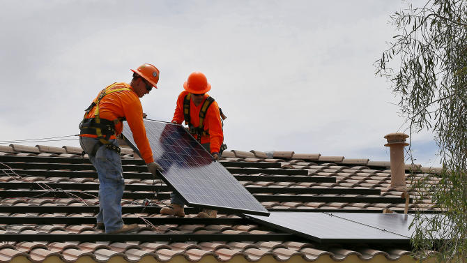 In this July 28, 2015, photo, electricians Adam Hall, right, and Steven Gabert, install solar panels on a roof for Arizona Public Service company in Goodyear, Ariz. Traditional power companies are getting into small-scale solar energy and competing for space. The emerging competition comes as utilities and smaller solar installers fight over the future of the U.S. energy system. (AP Photo/Matt York)