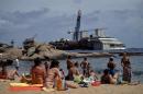 People sunbathe by the wrecked Costa Concordia cruise ship in Giglio Island on June 26, 2014