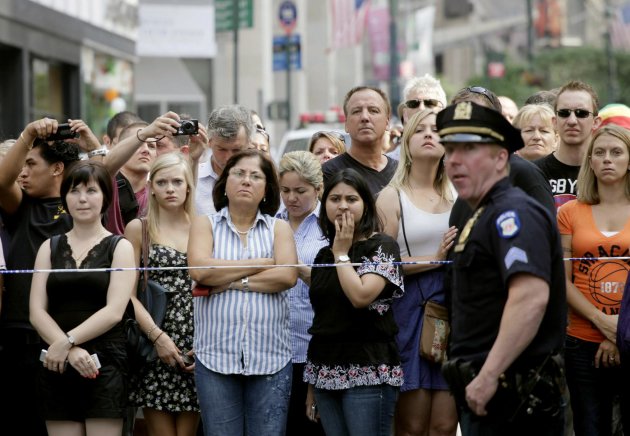 Bystanders and a police officer stand on Fifth Avenue to view the scene after a multiple shooting outside the Empire State Building, Friday, Aug. 24, 2012, in New York. At least four people were shot on Friday morning and the gunman was dead, New York City officials said. A witness said the gunman was firing indiscriminately. Police said as many as 10 people were injured, but it is unclear how many were hit by bullets. A law enforcement official said the shooting was related to a workplace dispute. The official spoke on condition of anonymity because the investigation was ongoing. (AP Photo/Mark Lennihan)