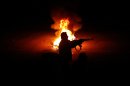 A Syrian rebel stands next to a flaming tire while firing at a Syrian army checkpoint, in a suburb of Damascus, Syria, on Saturday, March 17, 2012. Two suicide bombers detonated cars packed with explosives in near-simultaneous attacks on heavily guarded intelligence and security buildings in the Syrian capital Damascus Saturday, killing at least 27 people. (AP Photo)