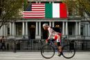A cyclist passes flags of the U.S. and Italy draped over the Eisenhower Executive Office Building beside the White House in Washington