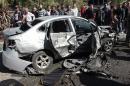 People gather around the wreckage of a car after a car bomb exploded in Homs