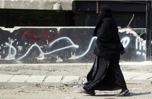 Egyptian veiled woman walk past a wall that reads 
