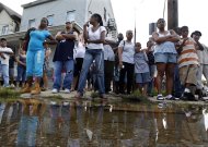 A crowd watches from a street corner Wednesday, Aug. 31, 2011, in Paterson, N.J., as New Jersey Gov. Chris Christie and Department of Homeland Security Secretary Janet Napolitano make a stop on a tour of areas flooded by Hurricane Irene. Later it was announced to the crowd that President Obama had signed a disaster declaration for hard-hit New Jersey after Hurricane Irene left much of  northern New Jersey flooded. (AP Photo/Mel Evans, Pool)