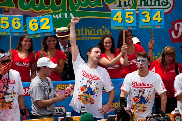 Four-time reigning champion Joey Chestnut, center, raises his arm in victory as he wins his fifth Nathan's Famous Hot Dog Eating World Championship with a total of 62 hot dogs and buns, Monday, July 4