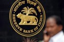 A man talks on his mobile phone as he walks past the logo of RBI inside its head office in Mumbai