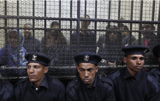 Egyptian policemen sit  in front of  Egyptian employees of several pro-democracy groups charged with using foreign funds to foment unrest during their trial in Cairo, Egypt, Sunday, Feb. 26, 2012. Egypt went forward with a trial Sunday that has plunged relations with the U.S. into the deepest crisis in decades, prosecuting 16 Americans and 27 other employees of pro-democracy groups. (AP Photo/Khalil Hamra)