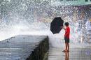 A boy holds an umbrella to a wave in Kailua-Kona on the island of Hawaii, Friday, Aug. 8, 2014. Iselle, the first tropical storm to hit the state in 22 years, knocked out power, caused flooding and downed trees when it crossed onto the Big Island in a rural and sparsely populated region. (AP Photo/Chris Stewart)