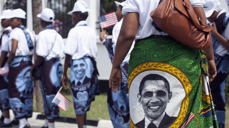 Young girls and women wear khangas, a traditional wrap, with the image of U.S. President Barack Obama as they line up to enter the State House, in Dar es Salaam, Tanzania, Monday, July 1, 2013, to greet and perform for U.S. President Barack Obama and first lady Michelle Obama. The Democratic president is due to fly into Dar es Salaam, Tanzania on Monday, the last stop on a weeklong tour of Africa that wraps up Tuesday, while his Republican predecessor coincidentally also plans to be there for a conference on African women organized by the George W. Bush Institute. (AP Photo/Carolyn Kaster)