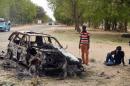 People stand by the wreckage of a car that has been blown up by suspected Boko Haram militants in Nigeria's troubled northeastern city of Maiduguri on March 25, 2014, killing five police officers, while a separate blast killed three
