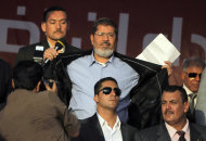 Egypt's President-elect Mohammed Morsi opens his suit jacket to show to his supporters that he is not wearing body armor at Tahrir Square, the focal point of Egyptian uprising, during his speech in Cairo, Egypt, Friday, June 29, 2012. Egypt's newly elected president has read that oath of office in Tahrir Square packed with tens of thousands of Islamists chanting against the ruling military council. In a strong-worded speech that meant to assuage popular
 anger at the military generals, Morsi showed defiance attempts to chip away from his own presidential powers. (AP Photo/Amr Nabil)