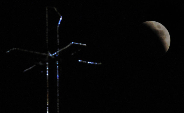 The moon is seen behind an illuminated cross of Ayios Nickolaos church during a lunar eclipse over  Nicosia, Cyprus, Wednesday, June 15, 2011. (AP Photo/Petros Karadjias)