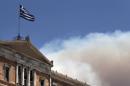 A Greek national flag flutters atop the parliament building as smoke from a raging wildfire rises in Athens