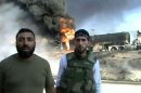 An image taken from a video uploaded on YouTube shows Syrian rebels standing in front of burning vehicles