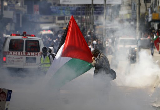An activist holds a Palestinian flag as he is surrounded by tear gas during clashes with Israeli security officers at a demonstration marking Land Day near Ramallah